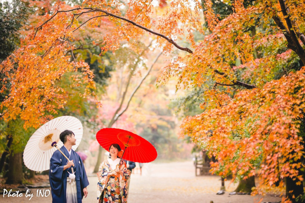 紅葉の時期に下鴨神社で番傘を指しながら歩く新郎新婦の前撮りの正面のカット